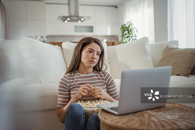 年轻女人坐在家里的地板上靠在沙发上看喜剧电影图片素材