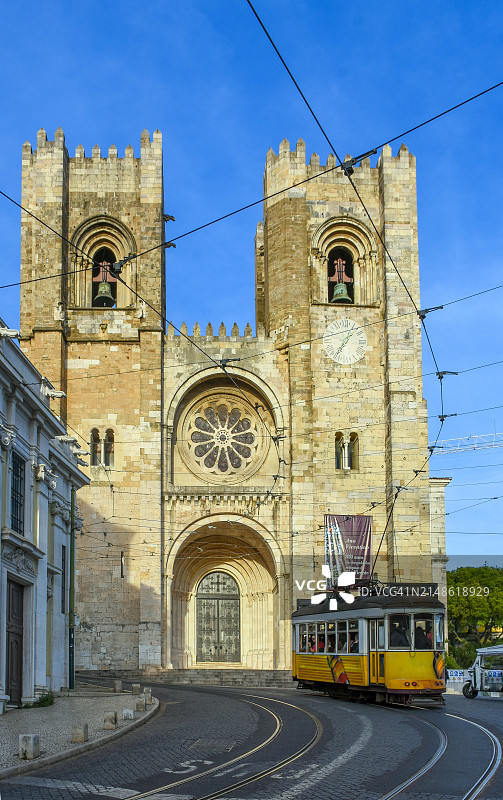 葡萄牙里斯本主教座堂日落时分的壮丽罗马式外观，以及传统黄色老式有轨电车图片素材