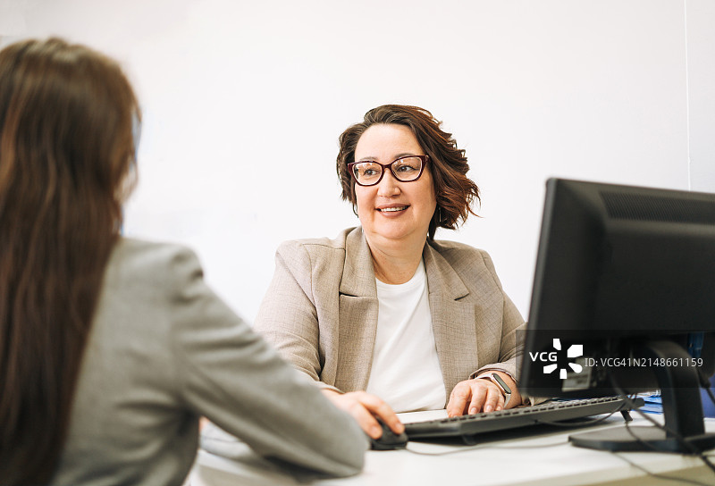 戴眼镜、穿西装的中年棕发女子在电脑前工作，并在办公室为客户提供建议图片素材