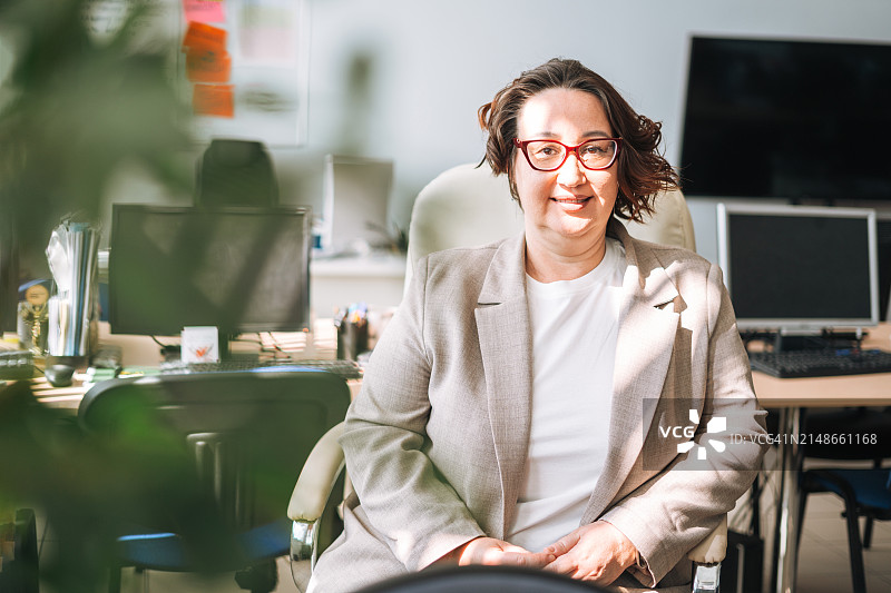 办公室里戴眼镜、穿西装的微笑中年棕发妇女肖像图片素材