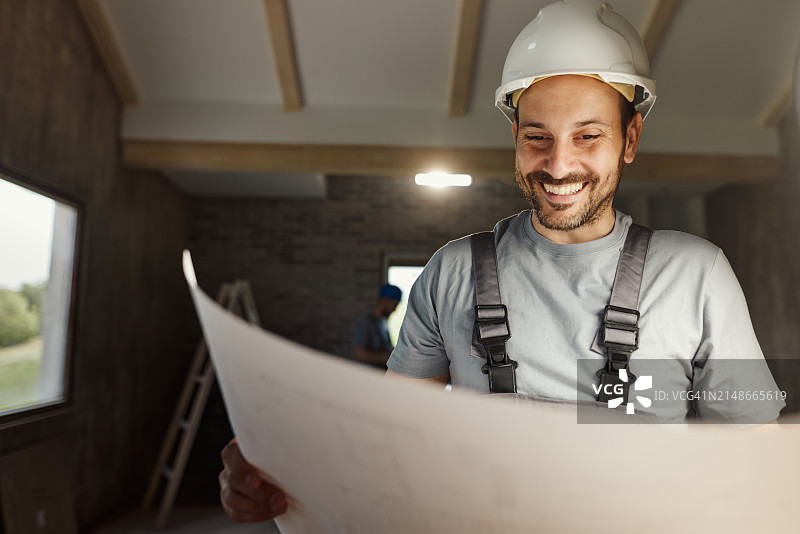 快乐的体力劳动者在房屋翻新过程中分析蓝图图片素材