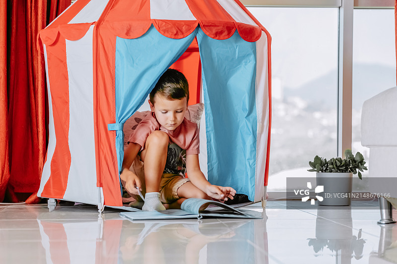 男孩在彩色游戏帐篷里靠窗阅读图片素材