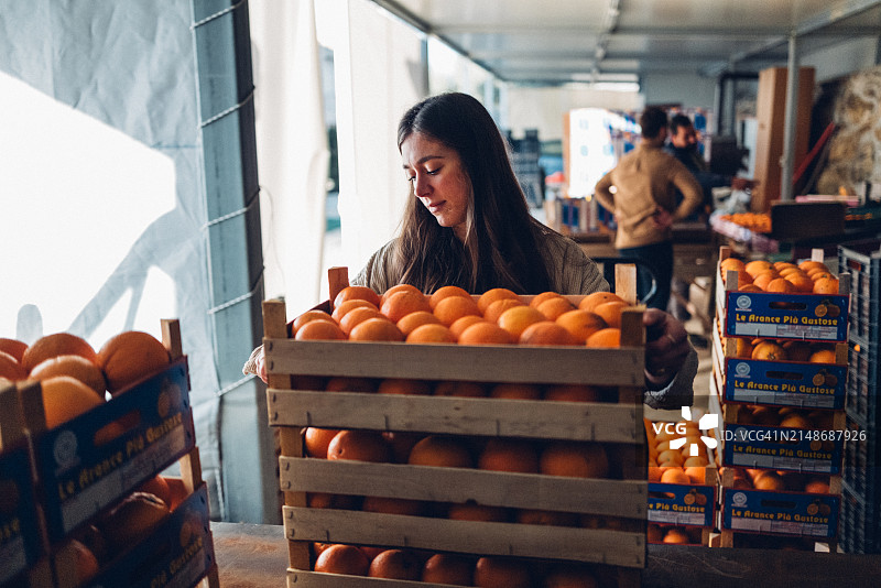 在仓库里抱着一箱橙子的女人图片素材
