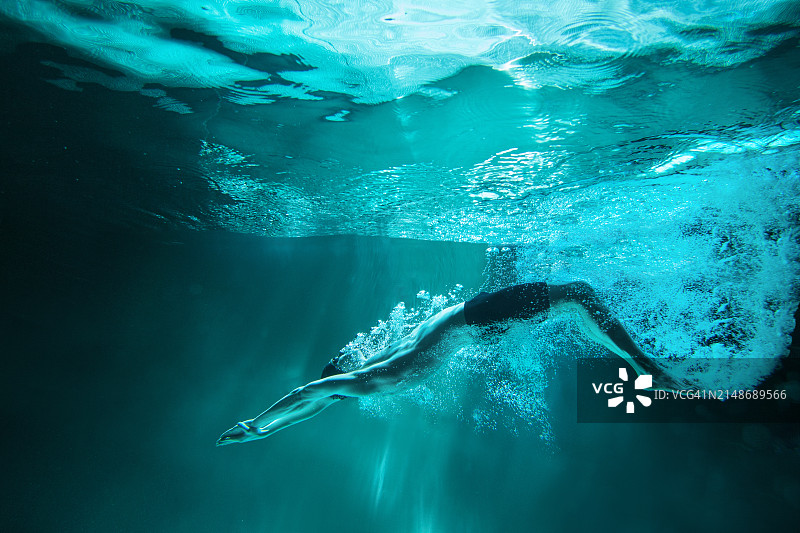 男运动员仰泳出发后在水下，深蓝色背景图片素材