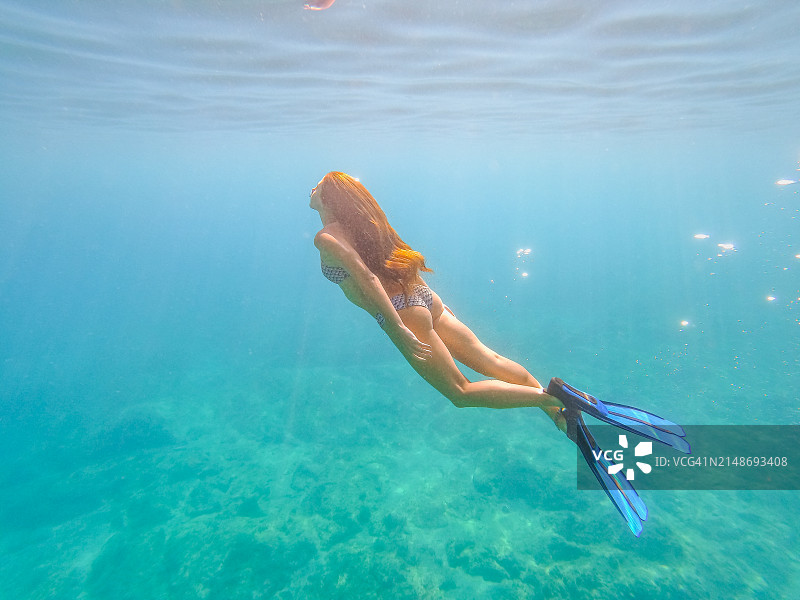 穿着比基尼和脚蹼在翠绿色海中潜水的漂亮女人，水下相机拍摄图片素材