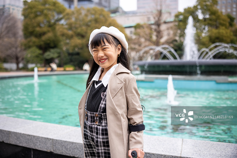 公园喷泉前拄拐杖的快乐小女孩肖像图片素材