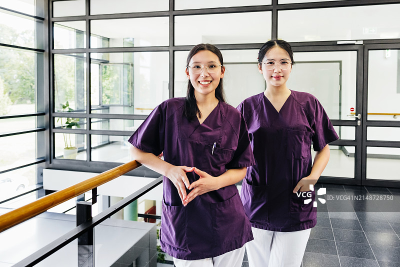 两位穿着工作服的年轻女医护人员站在明亮的医院走廊里图片素材