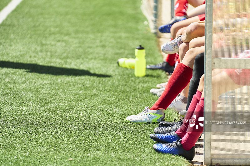 一群男孩穿着制服坐在足球场长凳上的腿部侧视图图片素材