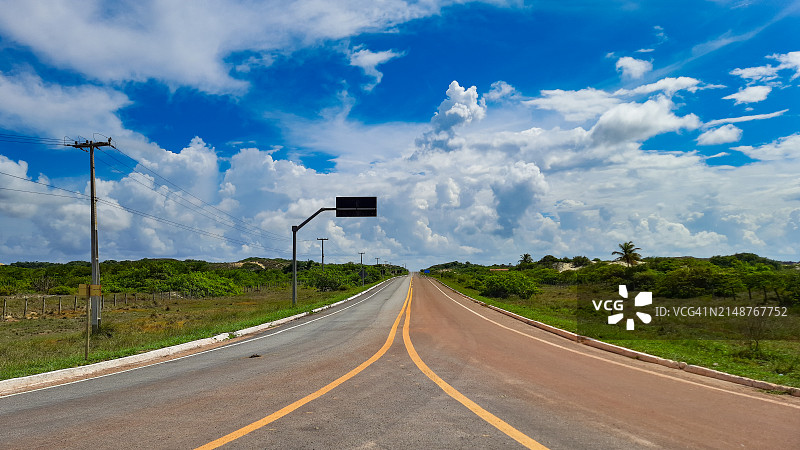 巴西东北部内陆的高速公路，路边有标志和排成行的柱子，蓝天与云朵交错。图片素材
