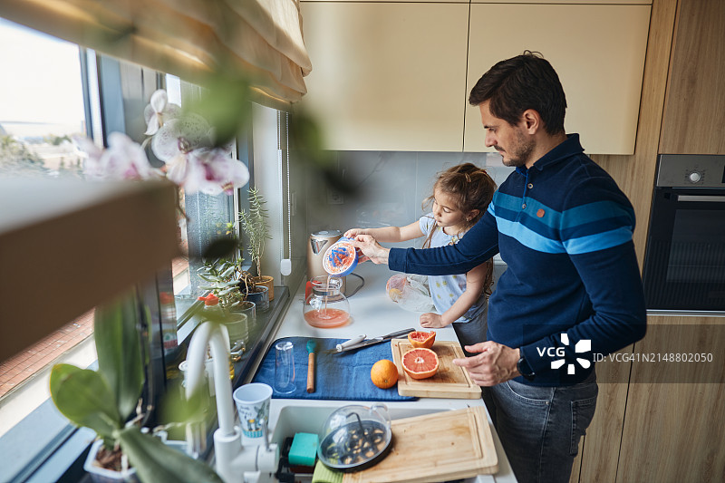 在厨房餐桌旁和父亲一起榨果汁的年轻女孩图片素材