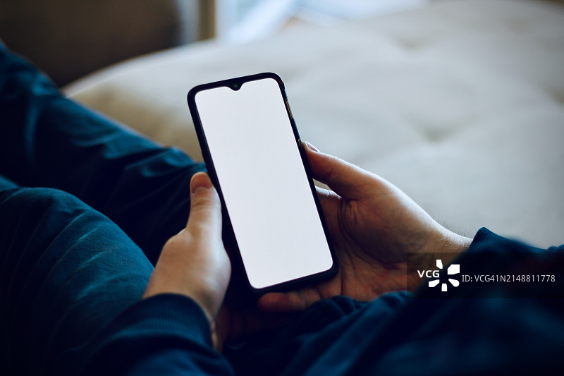 一个人在家中手持白色屏幕的移动设备图片素材
