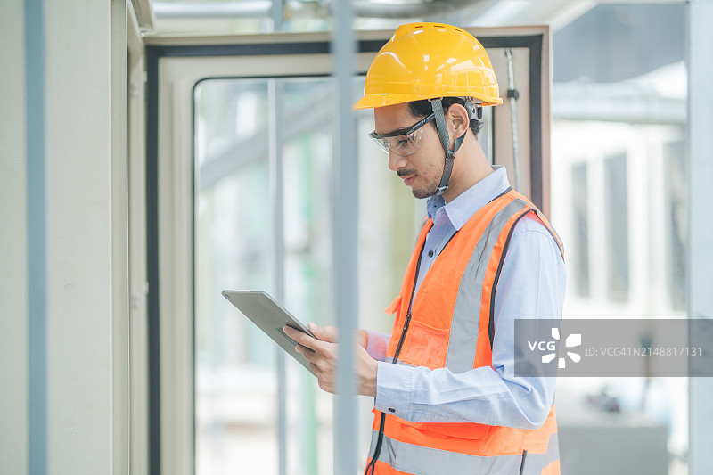 建筑工人戴安全帽和背心，在建筑工地使用平板电脑图片素材