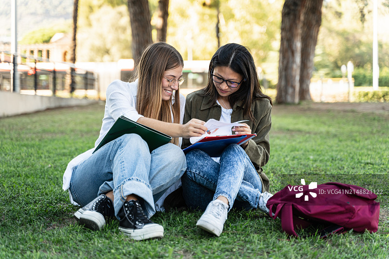 两个女学生朋友坐在大学校园的草地上一起学习图片素材