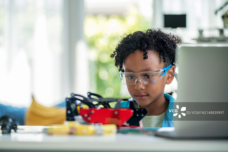年轻黑人男孩在家中通过遥控器积极参与线上电子学习，控制机器人的运动，展现好奇心、创造力和现代学习的创新精神图片素材