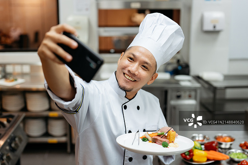 亚洲厨师在厨房用手机录制烹饪视频博客图片素材