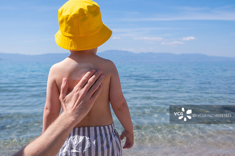 父亲在沙滩上给孩子背部涂抹防晒霜图片素材
