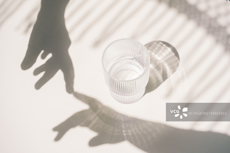 白色桌子上，手触碰着有阴影的水杯图片素材