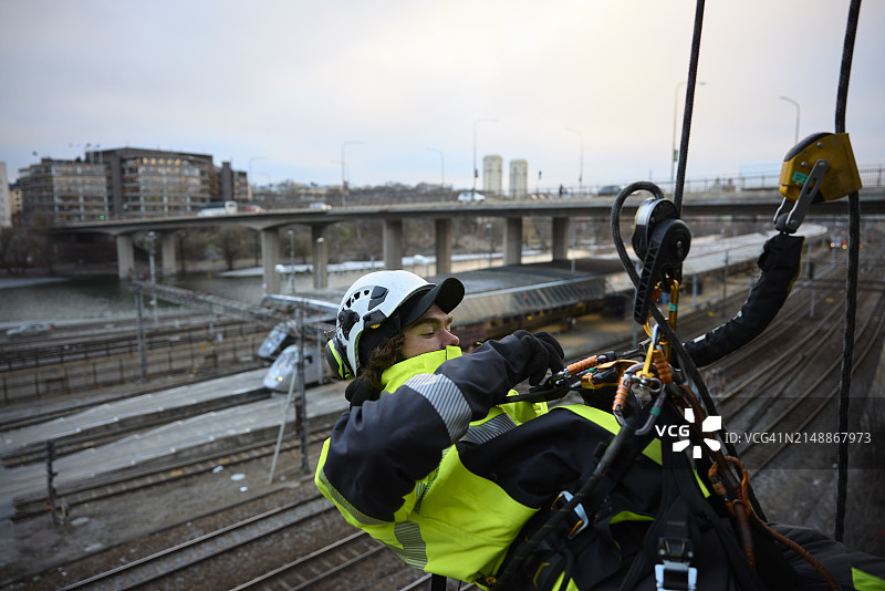 高空作业工人将登山扣固定在绳索上，悬挂在铁轨上方图片素材