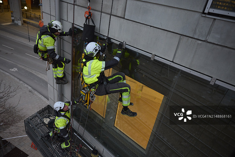 高空作业工人安装建筑物窗户的高角度景观图片素材