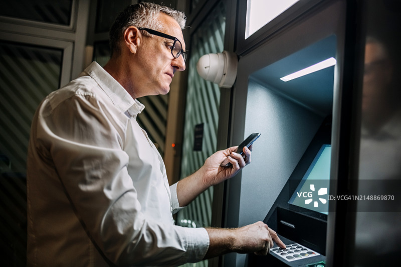 夜晚在ATM机前使用手机的单人。图片素材