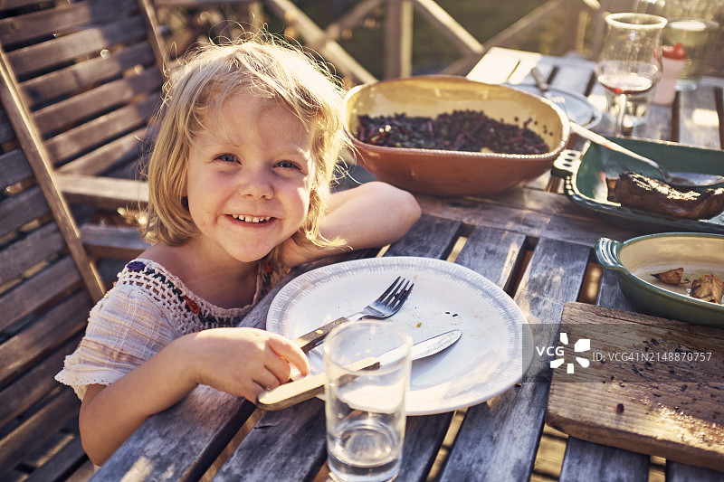 笑容甜美的女孩坐在桌旁，面前是空盘子图片素材