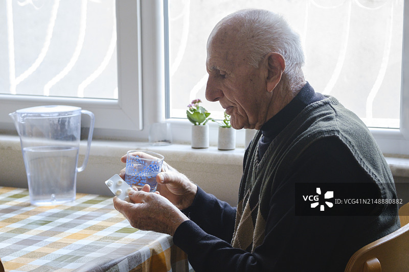 坐在厨房吃药的年长男人的肖像图片素材