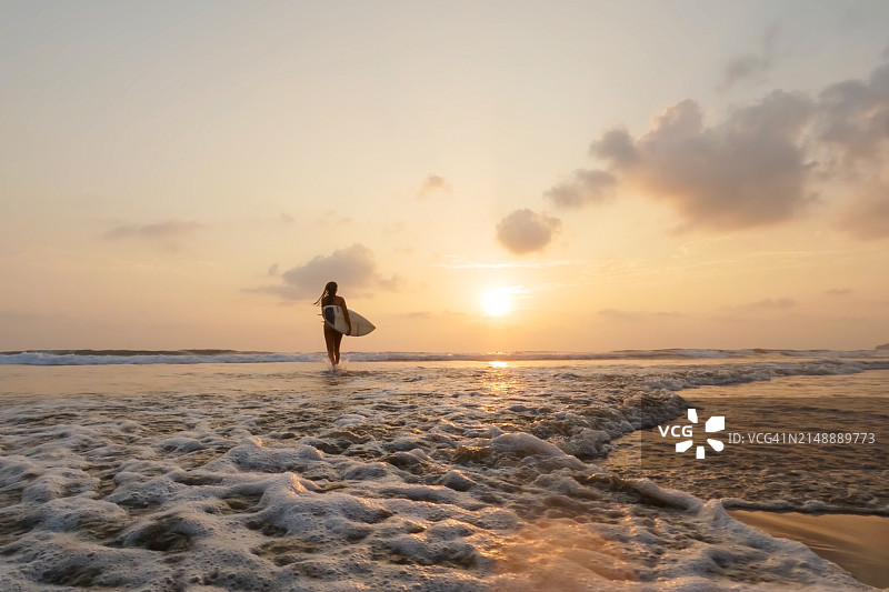 低角度日落海滩冲浪的女人图片素材