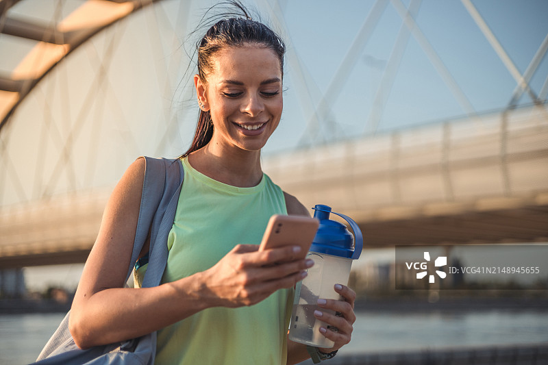 在户外用手机发短信的年轻女运动员图片素材