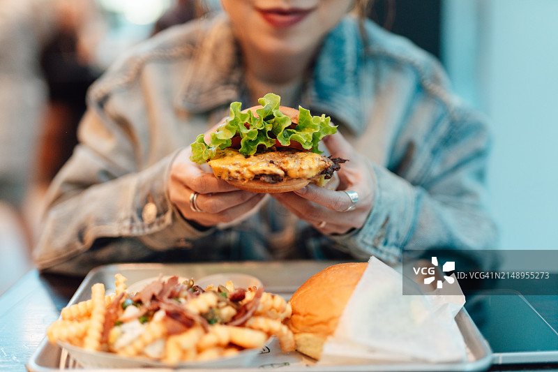 年轻亚裔女性在餐厅吃汉堡和薯条的特写图片素材