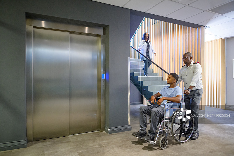 男护士在医院电梯处推着坐轮椅的男病人，女医生从楼梯上下来图片素材