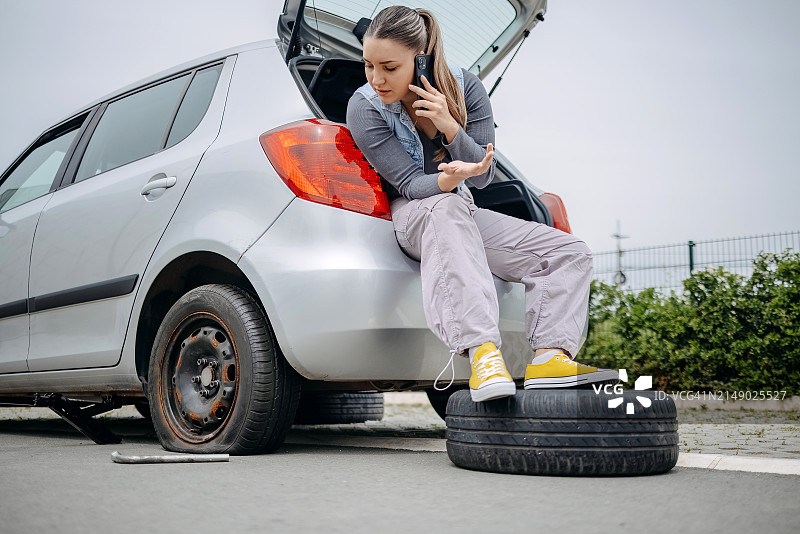女人坐在车后，用手机寻求帮助，因为轮胎没气了图片素材