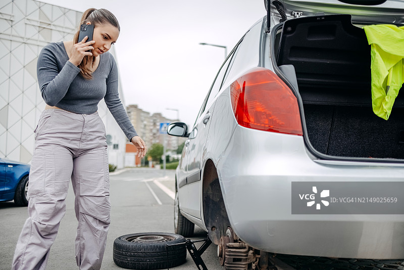 女人在路上轮胎没气，使用手机寻求帮助图片素材