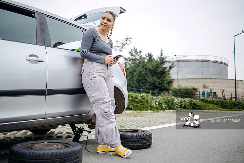 女人在路上轮胎没气，使用手机寻求帮助图片素材