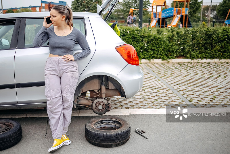女人在路上轮胎没气，使用手机寻求帮助图片素材