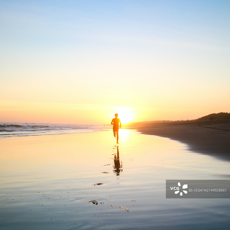 日落时在海滩上奔跑的男孩轮廓图片素材