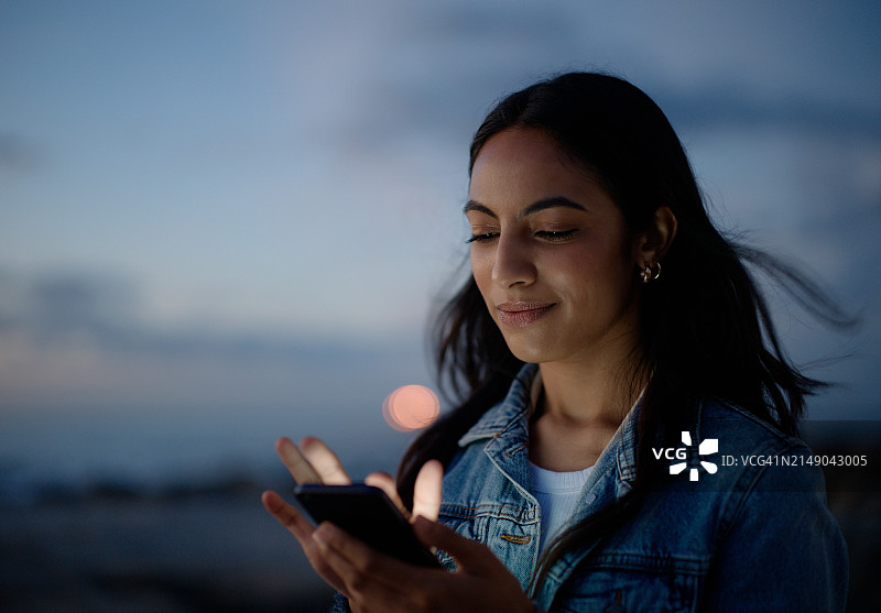户外：夜晚使用智能手机浏览社交媒体的女性图片素材