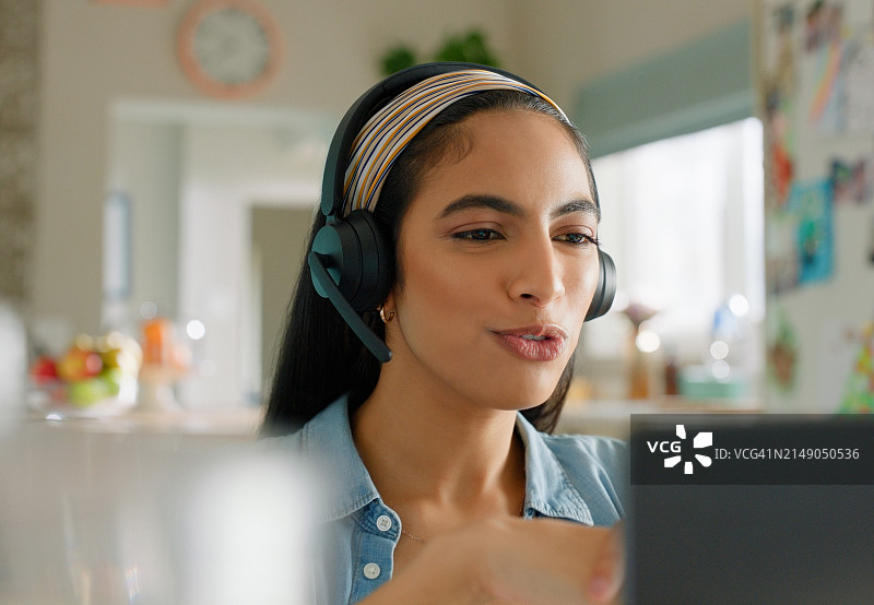 居家办公：通过电脑进行沟通、辅导和在线学习的女性导师。戴着耳机为学生提供知识反馈、测试或考试的在线教师图片素材