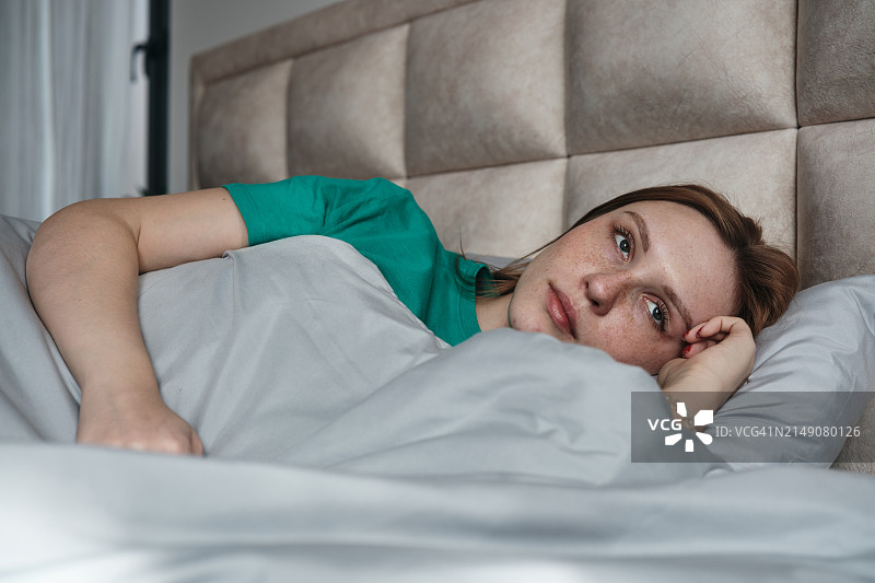 悲伤的女人躺在床上看着窗外。早晨的沮丧图片素材