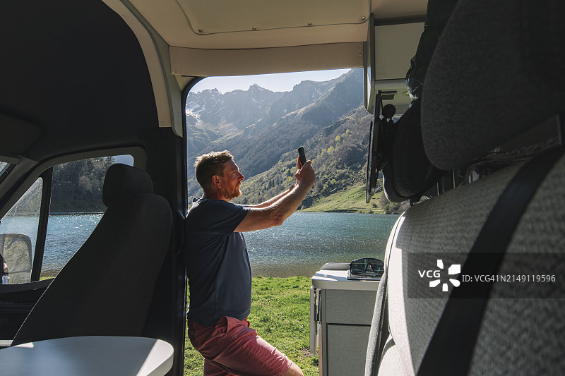 中年男人在法国比利牛斯山脉的房车里拍摄美丽的湖景图片素材