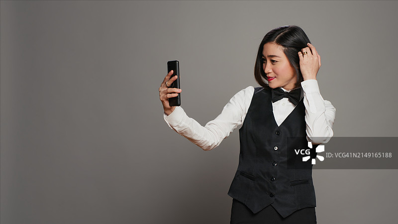 对着灰色背景使用手机的微笑年轻女商人图片素材
