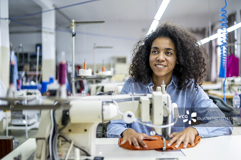 年轻的非裔美国女裁缝在时装工作室使用现代缝纫机工作图片素材
