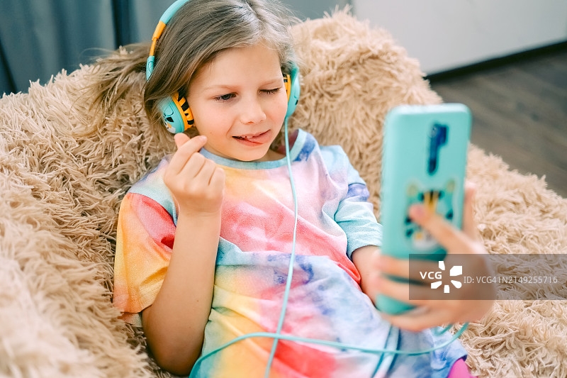在家躺在沙发上使用手机和耳机的少女图片素材