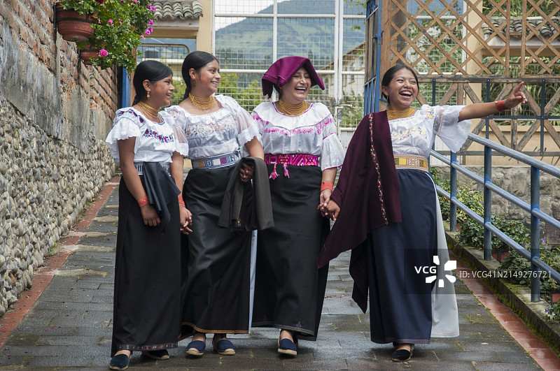 四位身着传统服饰的女士在迷人的街道上欢笑同行图片素材