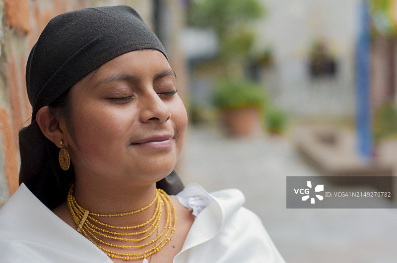 来自厄瓜多尔的年轻漂亮土著妇女闭着眼睛微笑，享受温暖的阳光，身着手工刺绣的民族服装图片素材