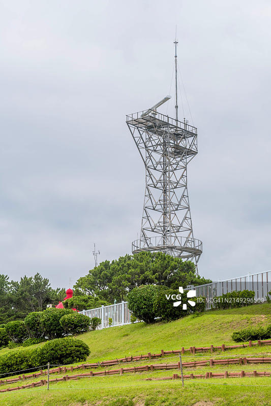韩国蔚山，多云天空下郁郁葱葱的绿色植物中的高大金属雷达塔图片素材