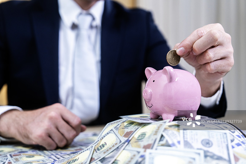 年轻亚洲商人将硬币放入存钱罐图片素材