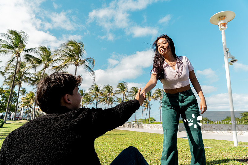年轻女人在公园里帮助男朋友从地上站起来图片素材