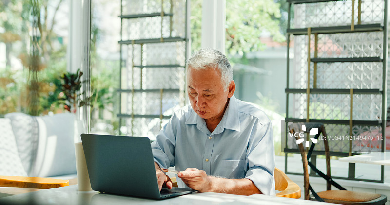 年长的亚洲男性在咖啡馆轻松地用笔记本电脑支付信用卡，非接触式支付图片素材