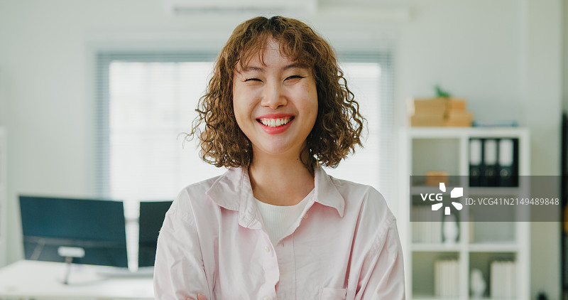 微笑的年轻亚洲女商人，一头卷发，自信地站在办公环境中，象征着专业和成功。ESG可持续商业办公室。图片素材