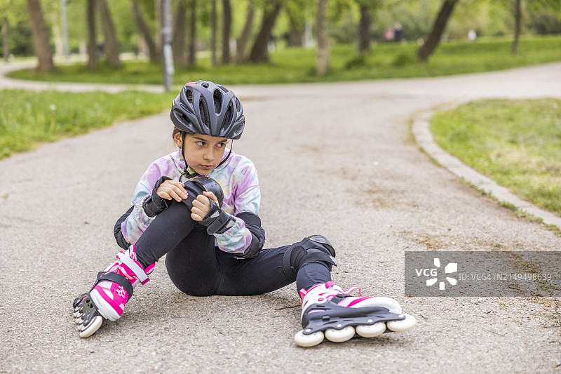 一个穿着防护装备的 школьница 在公共公园里玩轮滑时不小心摔倒在沥青路面上图片素材